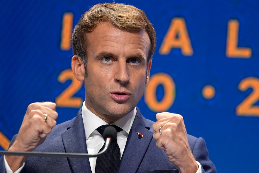 French President speaks at microphone holding hands in fist.