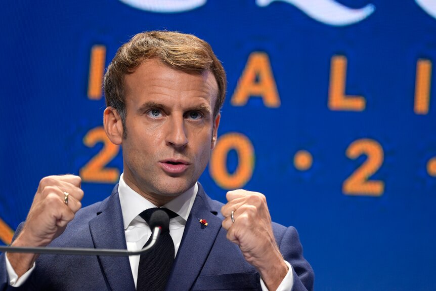 French President speaks at microphone holding hands in fist.