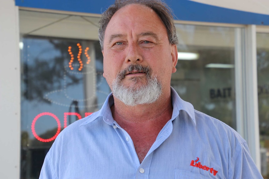 A headshot of a man with a blue shirt with a logo on it in front of a roadhouse cafe.