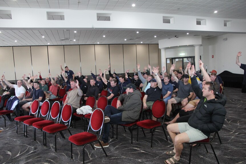 A roomful of men raise their hands as part of a vote.