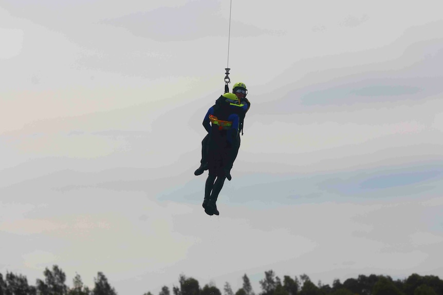 Woman hanging from harness from aircraft holds onto another person.