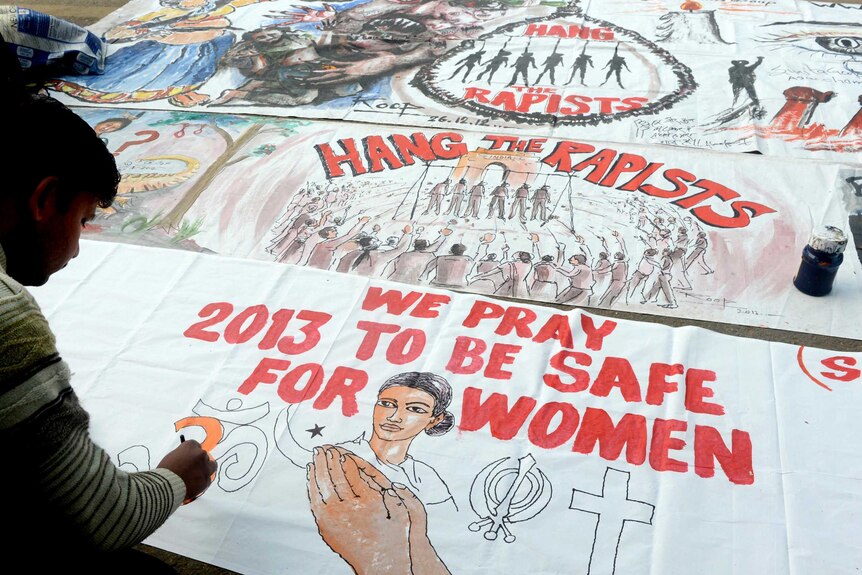 A bystander writes on a banner supporting the hanging of the rapists.