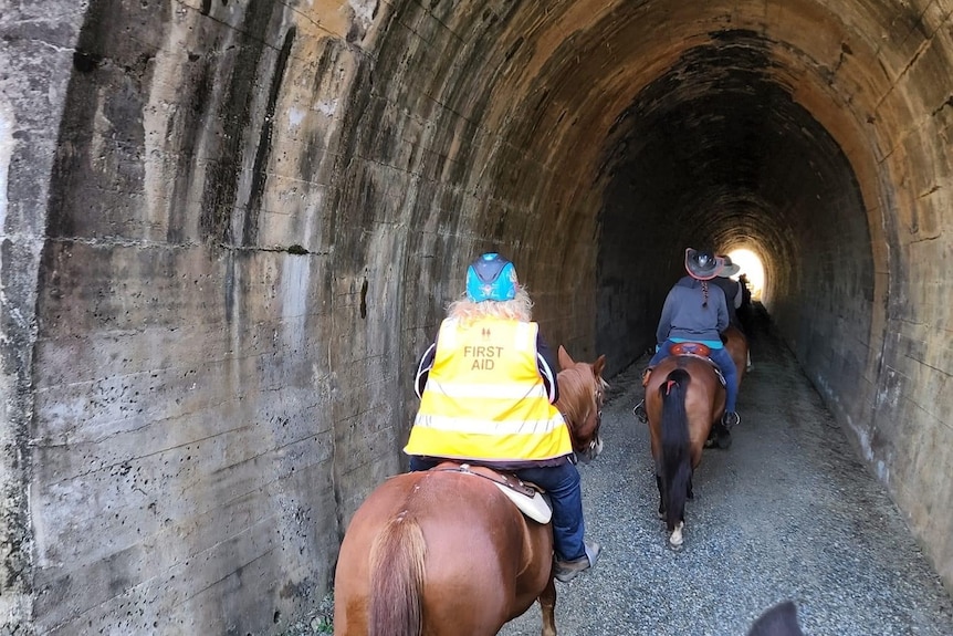 riders on horses ride through a tunnel 