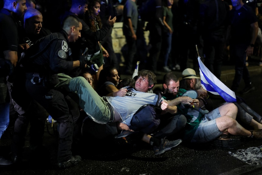 A man, who is lying on his back and surrounded by other people, looks at a police officer.