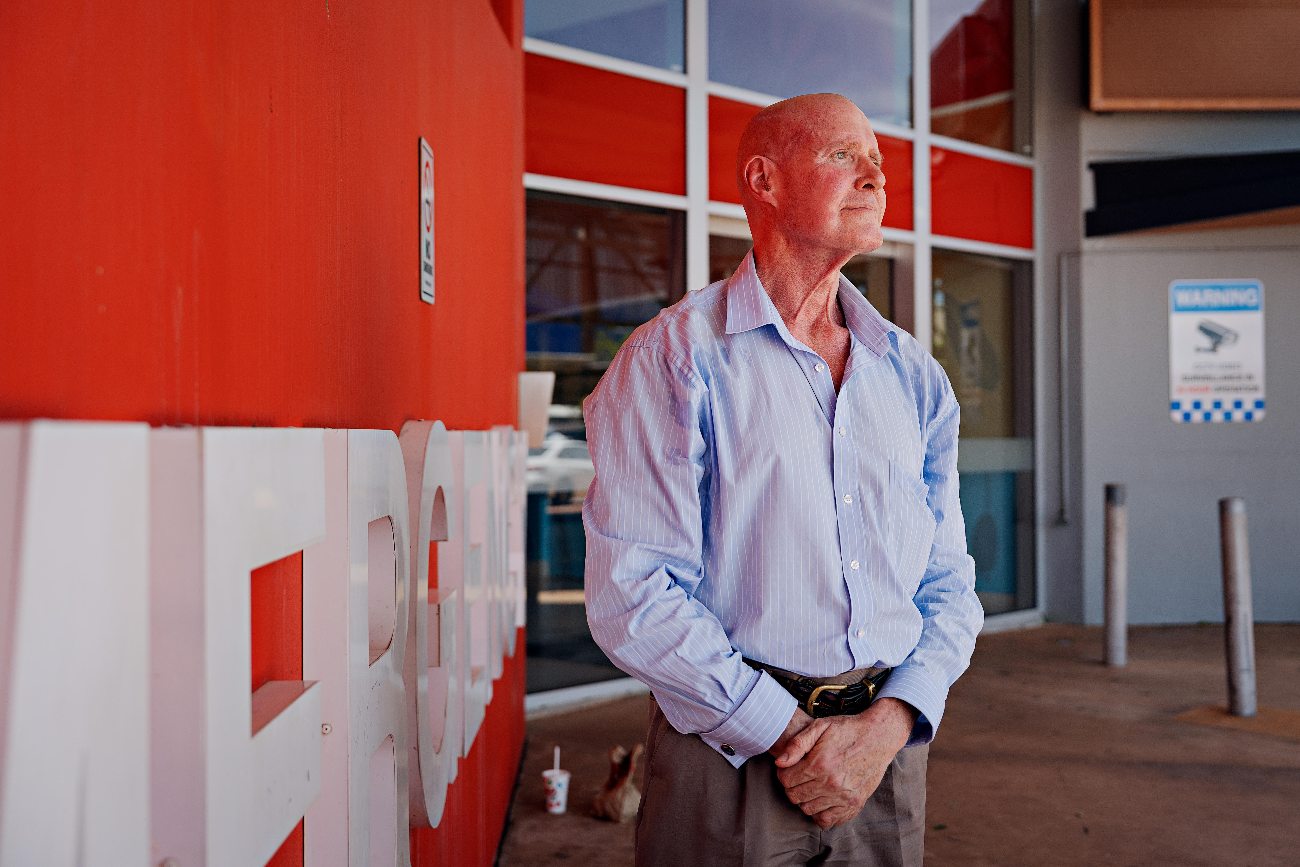 Un hombre con una camisa azul claro se encuentra frente a un hospital con una expresión seria.