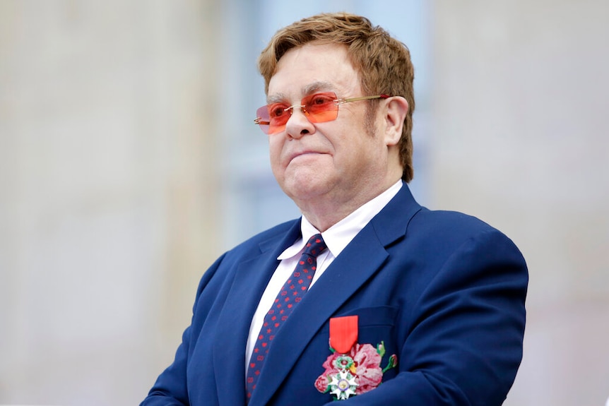 Elton John wearing a suit and a medal on his suit jacket.