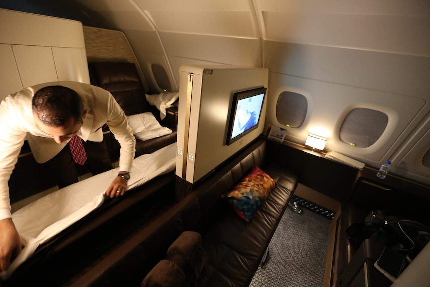 A dimly-lit first-class Etihad Airways cabin shows an flight attendant making up someone's lounge.