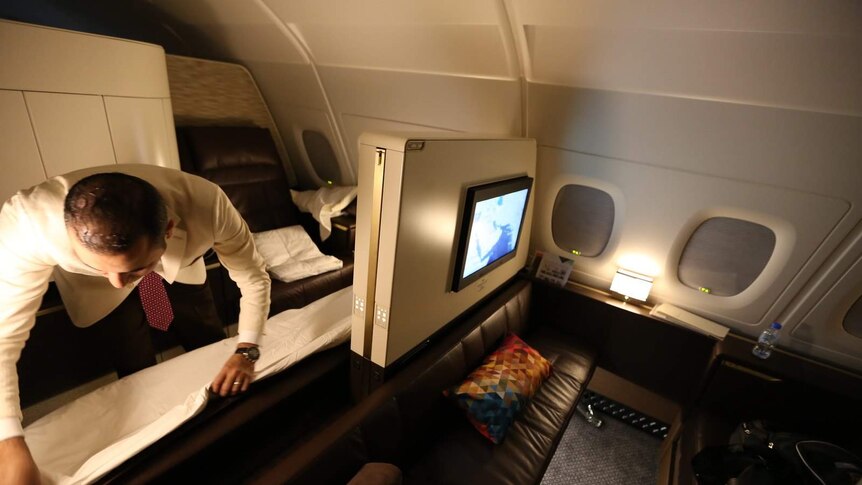 A dimly-lit first-class Etihad Airways cabin shows an flight attendant making up someone's lounge.