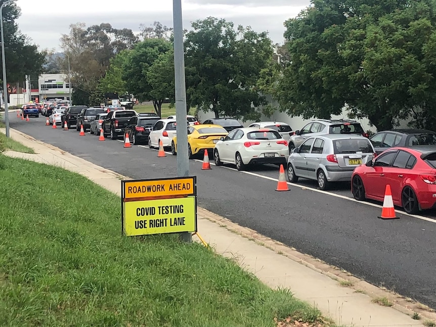 Cars queue along a road near a sign reading 'COVID testing use right lane'.