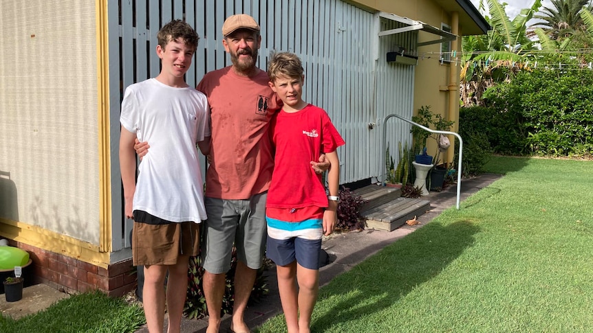 Two teenagers with man in hat standing out the front of house