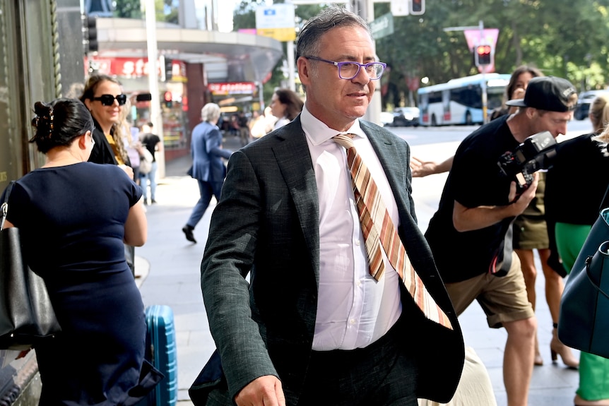 Man in suit and glasses walks out of court