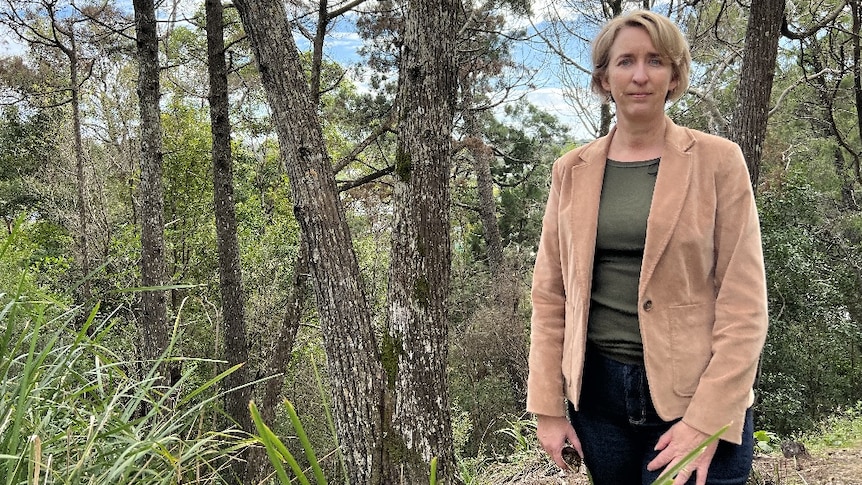 Woman in brown jacket standing with trees.