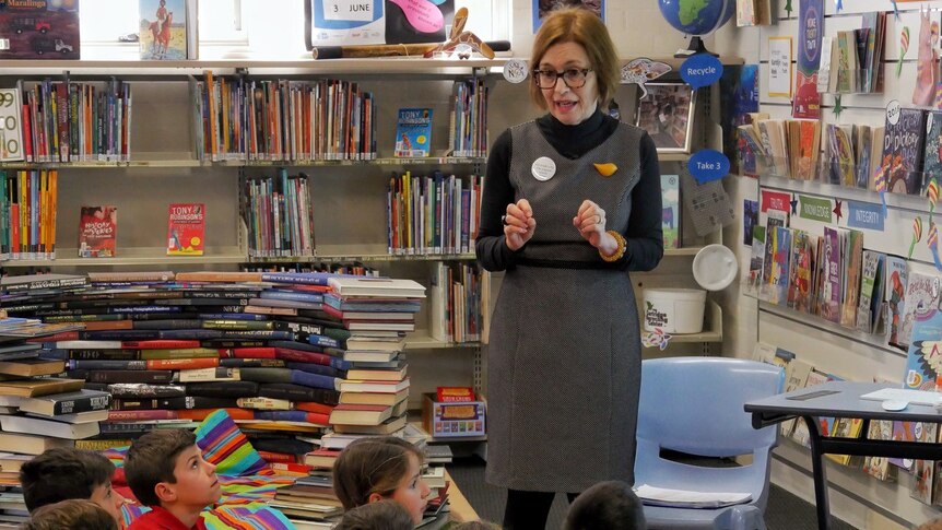 A teacher librarian chats to children sitting on the floor of the library.