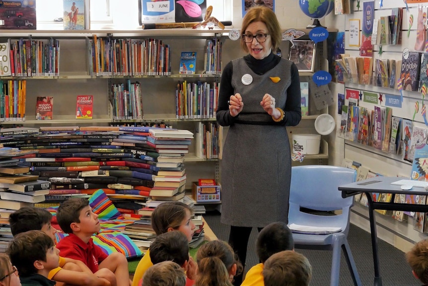 A teacher librarian chats to children sitting on the floor of the library.