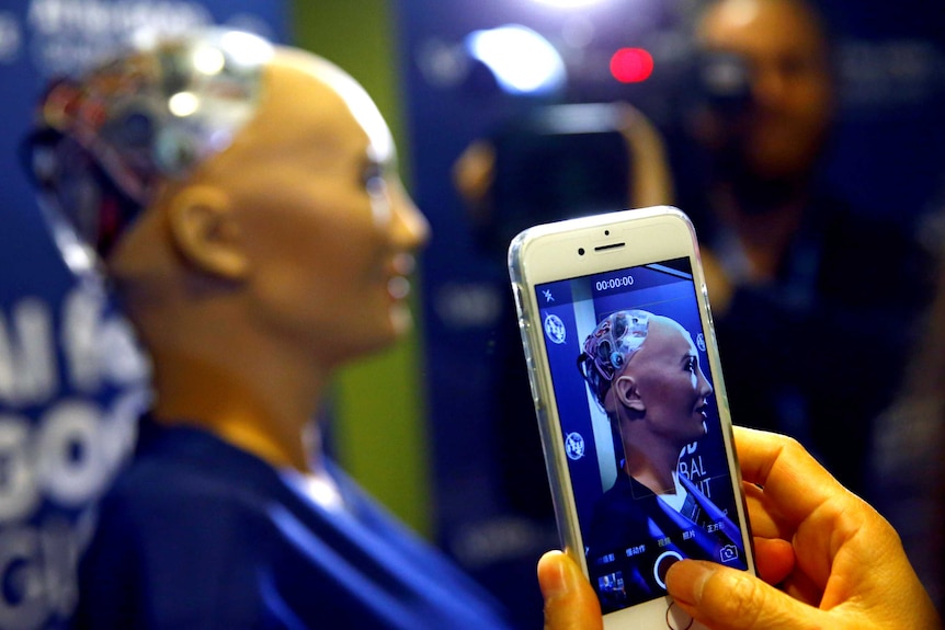 A hand holding a phone takes a photo of a robot