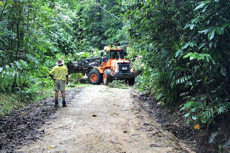 A front end loader clears fallen trees on a narrow dirt road in far north Queensland.