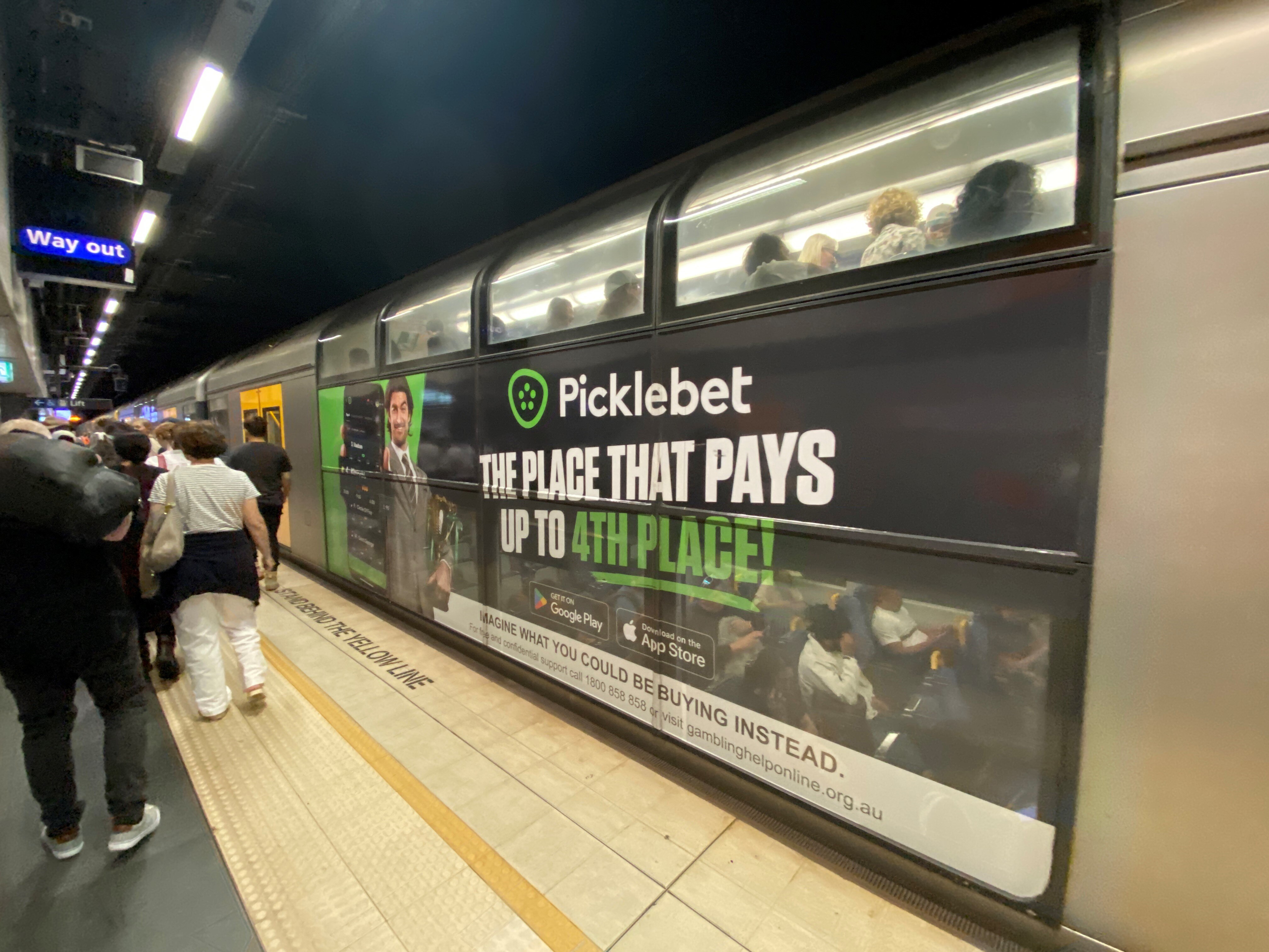 A gambling ad on the side of a train as commuters walk past.