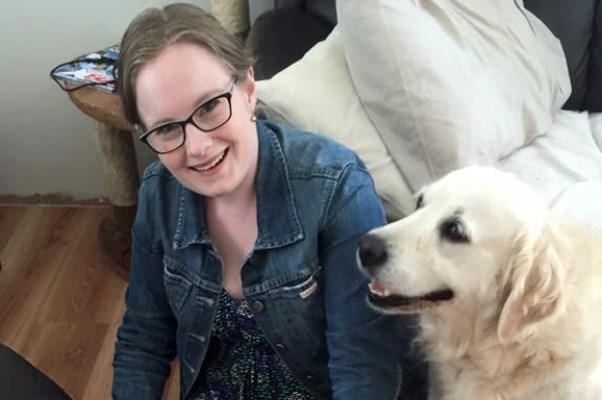 Emily is smiling and sitting on the floor with three golden retriever dogs.
