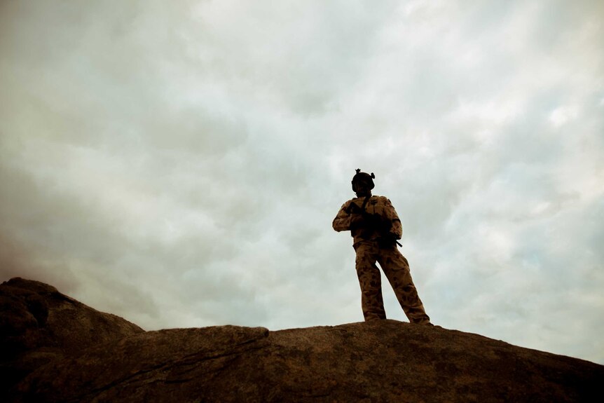 A silhouette of an armed soldier standing on rocks.