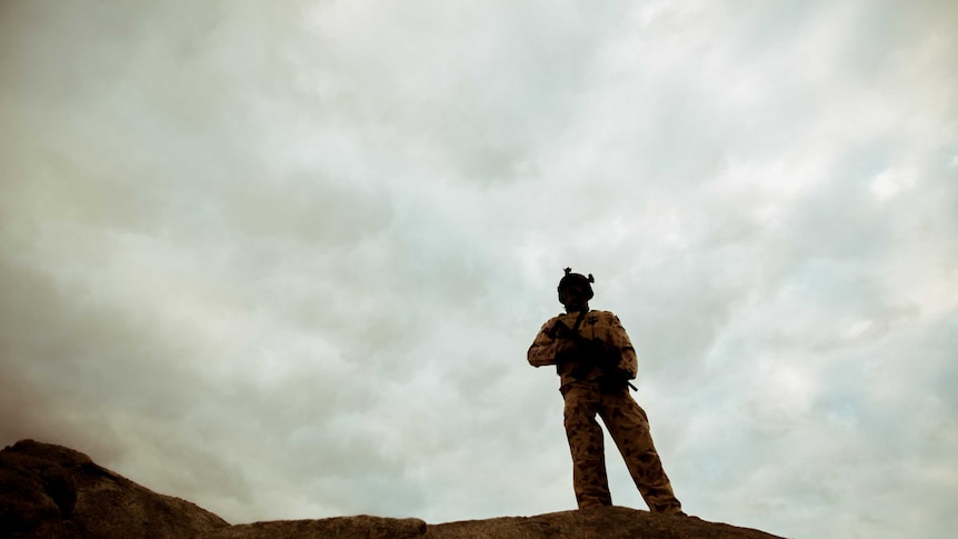 A silhouette of an armed soldier standing on rocks.