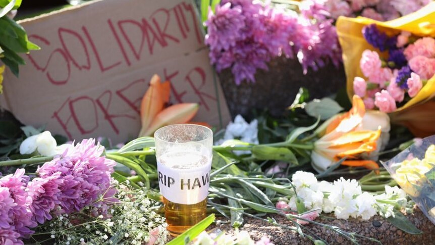 A pint of beer with the label RIP HAWKE is left in a throng of flowers on the Opera House steps.