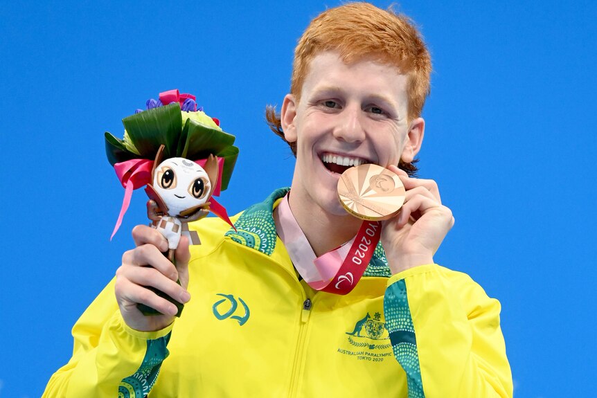 Man stands biting on bronze medal