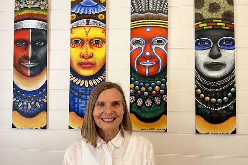 A smiling woman stands in front of 4 colourful pictures.