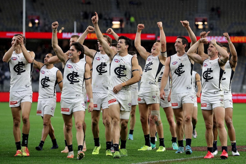 A group of Carlton AFL players wave to their supporters in the stands.