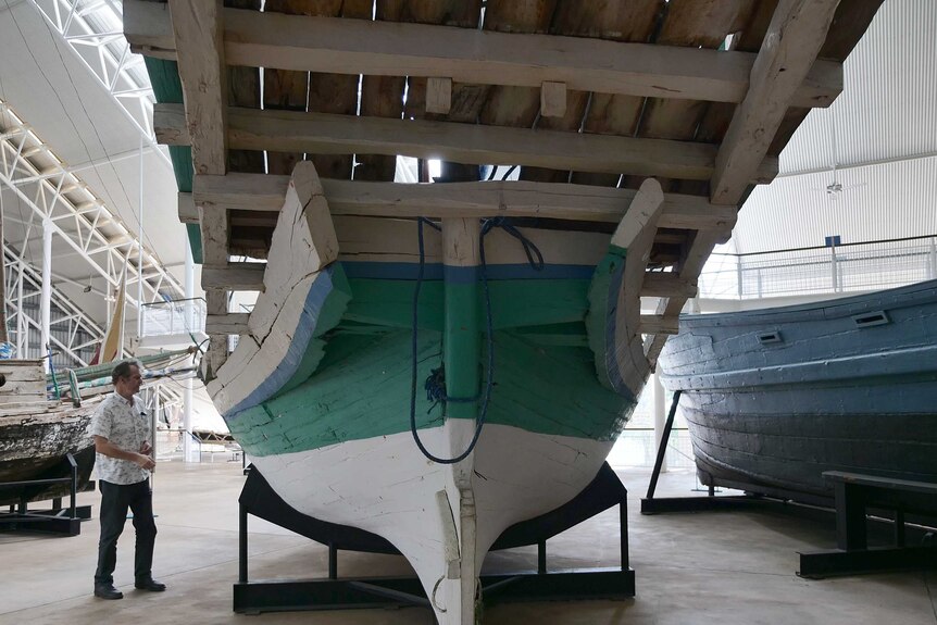 A man studies the bottom of a timber boat.