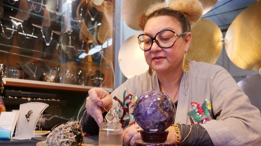 Ms Campbell dips a diamond ring into a jar of salt water, while smoking sage and amethyst crystals sit nearby