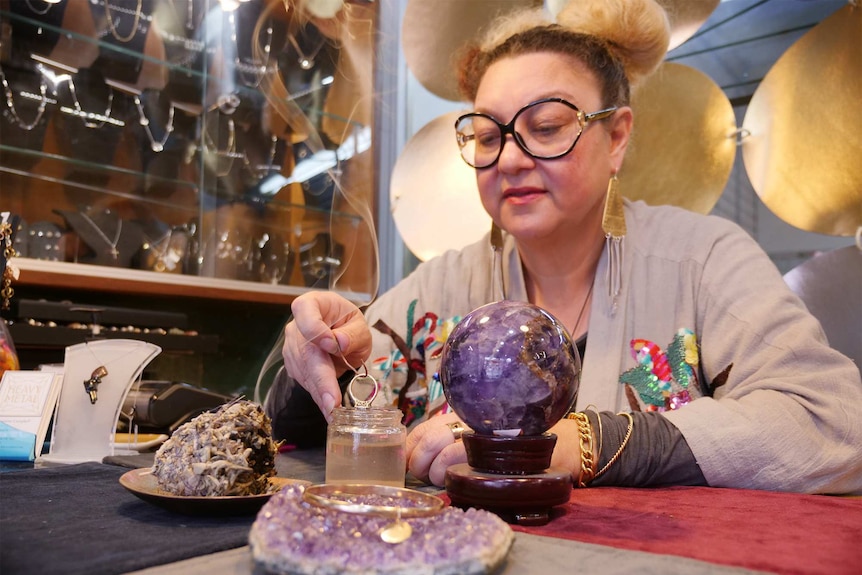 Ms Campbell dips a diamond ring into a jar of salt water, while smoking sage and amethyst crystals sit nearby