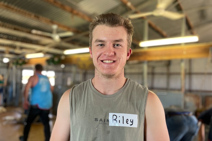 A young boy in a singlet stands in a shearing shed.