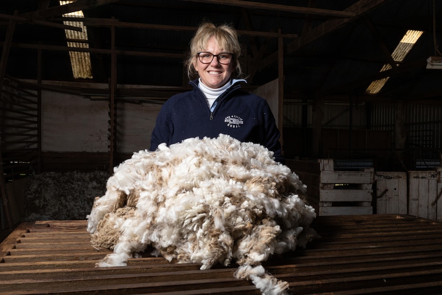 A woman stands behind a pile of clipped wool