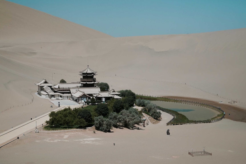 Traditional Chinese buildings sit on the side of an oasis in the Gobi desert