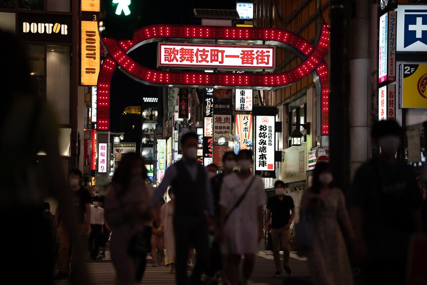 A Tokyo laneway lit up by neon signs with many pedestrians walking through 