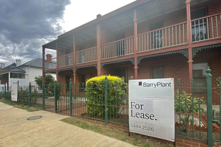 A block of brown social housing with a real estate sign out the front.