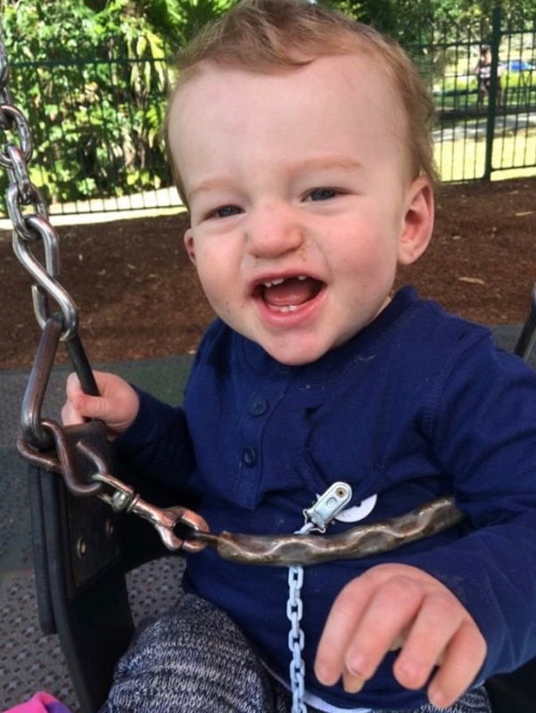 21-month-old Corby Akehurst smiling and sitting on swing.