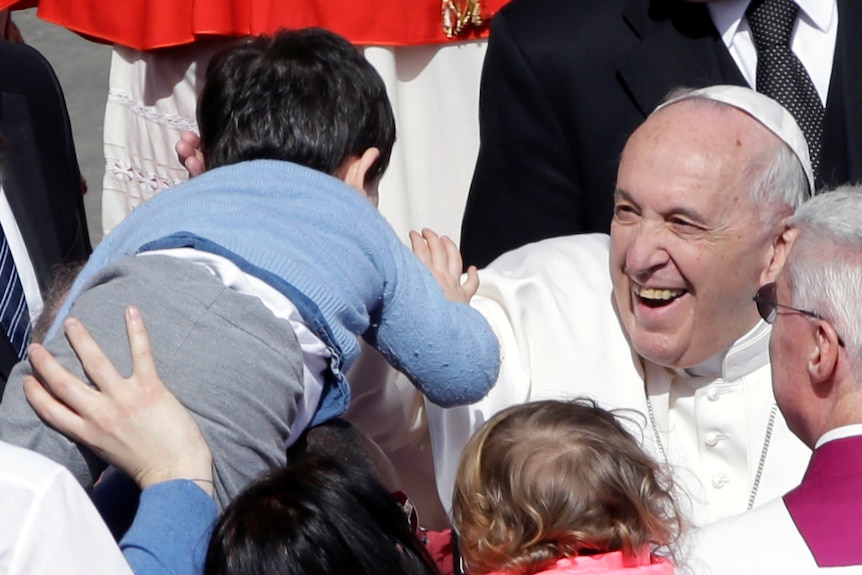 Pope Francis looks thrilled as he embraces a child as he makes his way through the crowd