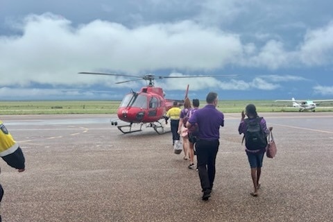A group of people walking towards a helicopter on airstrip.