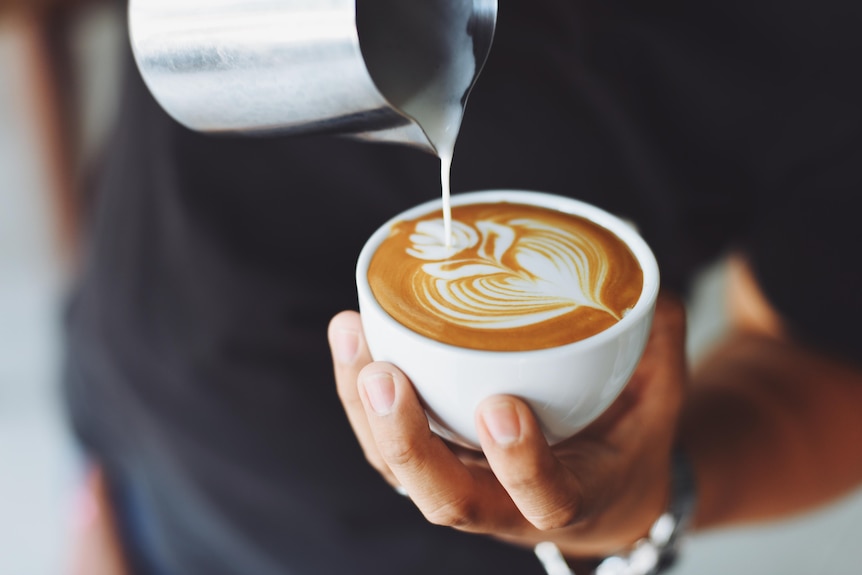 A person pours milk into a cup with coffee.
