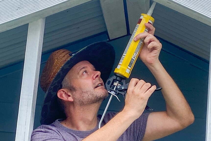 Tim Lawson holds a caulking gun while working on a house.