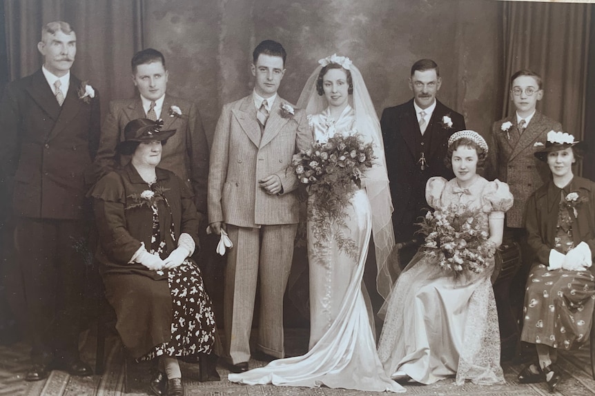 A black and white group photo of a wedding party with the bride and groom in the centre.