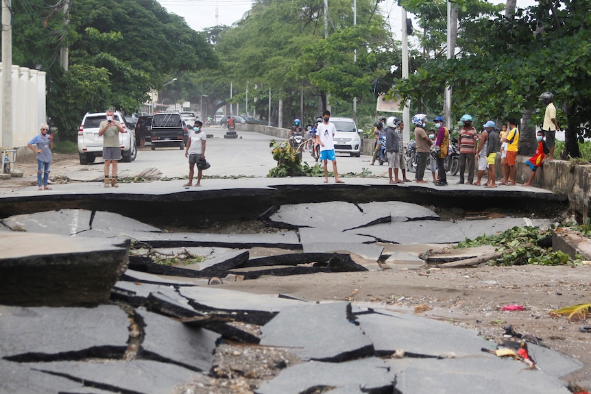 People inspect the remains of an asphalt road that was destroyed by heavy rain and flooding.