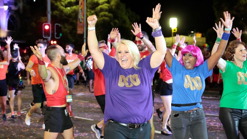 Manda in a street parade with other ABC staff. They are wearing bright tshirts with a gold lissajou print and looking very happy