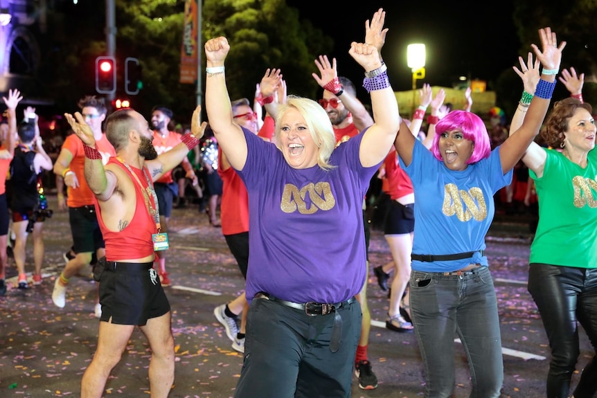 Manda in a street parade with other ABC staff. They are wearing bright tshirts with a gold lissajou print and looking very happy
