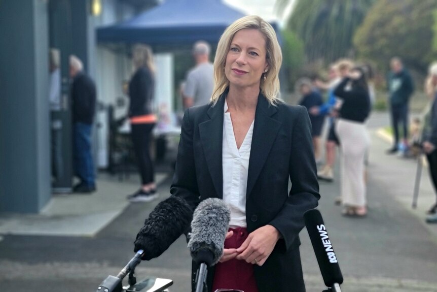 A blonde woman fronts the microphones outside a polling booth.