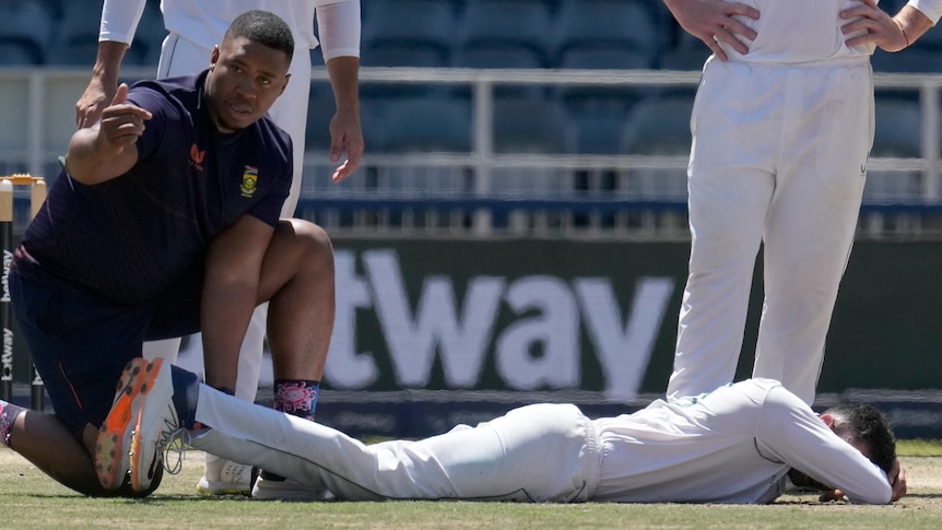 Keshav Maharaj lies on the ground clutching his head while receiving attention 