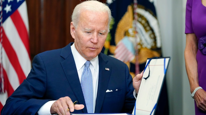 President Joe Biden sitting and holding open the file to sign.