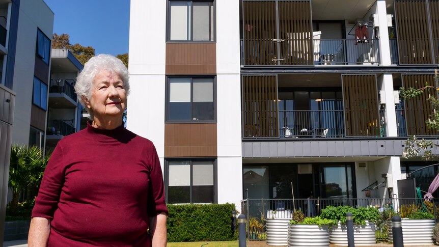 A woman with grey hair and a maroon top outside a modern apartment building