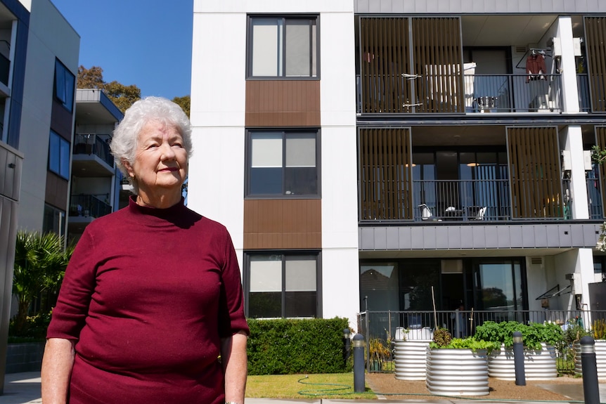 A woman with grey hair and a maroon top outside a modern apartment building